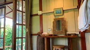 Una habitación rústica con vigas de madera, un taburete de madera, una mesita con un espejo y una ventana con cortinas.