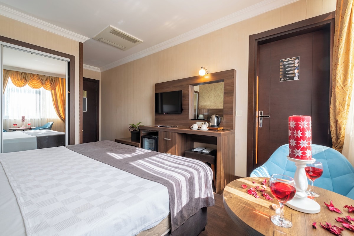 Habitación de hotel con cama, escritorio, televisión y zona de comedor con mesa y sillas.