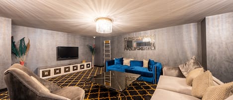 A modern living room with a large flat-screen TV, a blue sofa, and a patterned carpet.