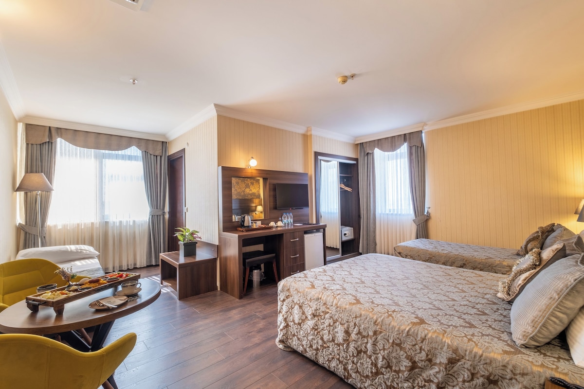 A hotel room with a bed, desk, chair, and a small dining table with a tray of food.