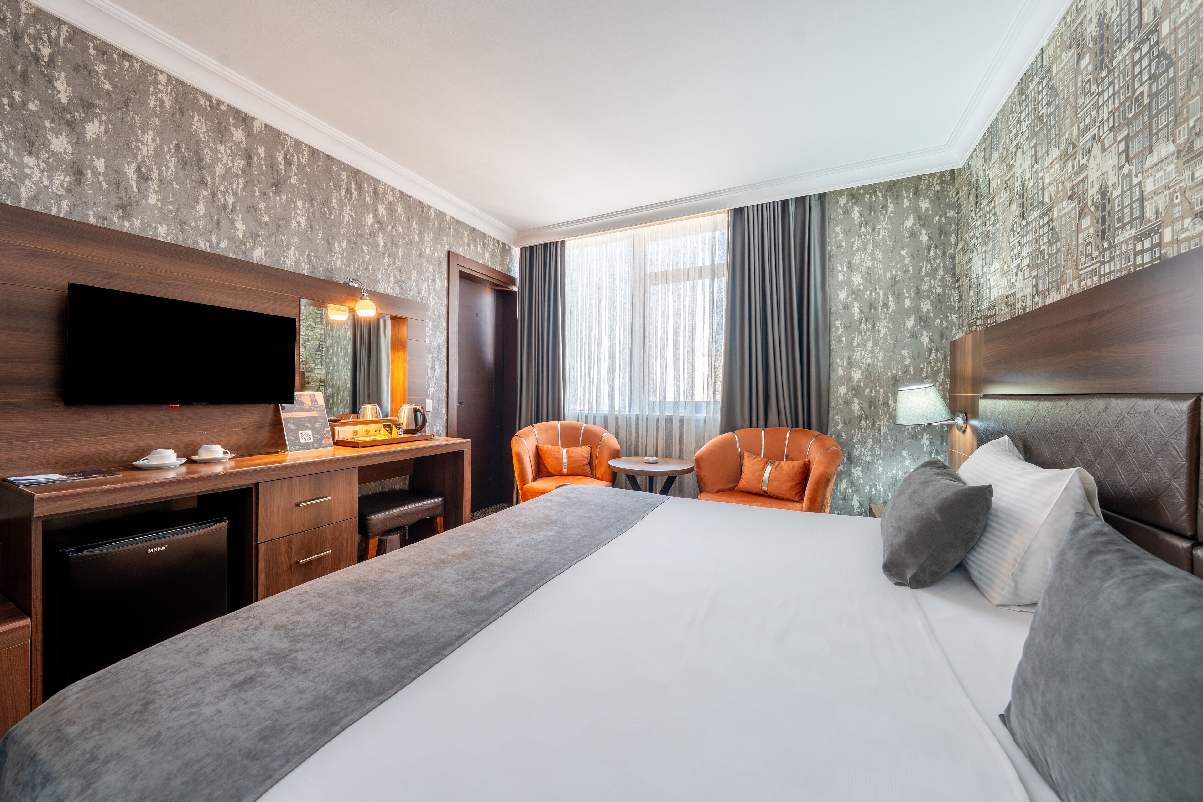Una habitación de hotel con cama, escritorio, silla, televisor y ventana con cortinas.