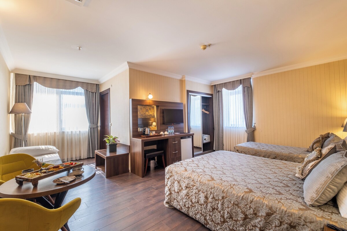A hotel room with a bed, desk, chair, and a small dining table with a tray of food.