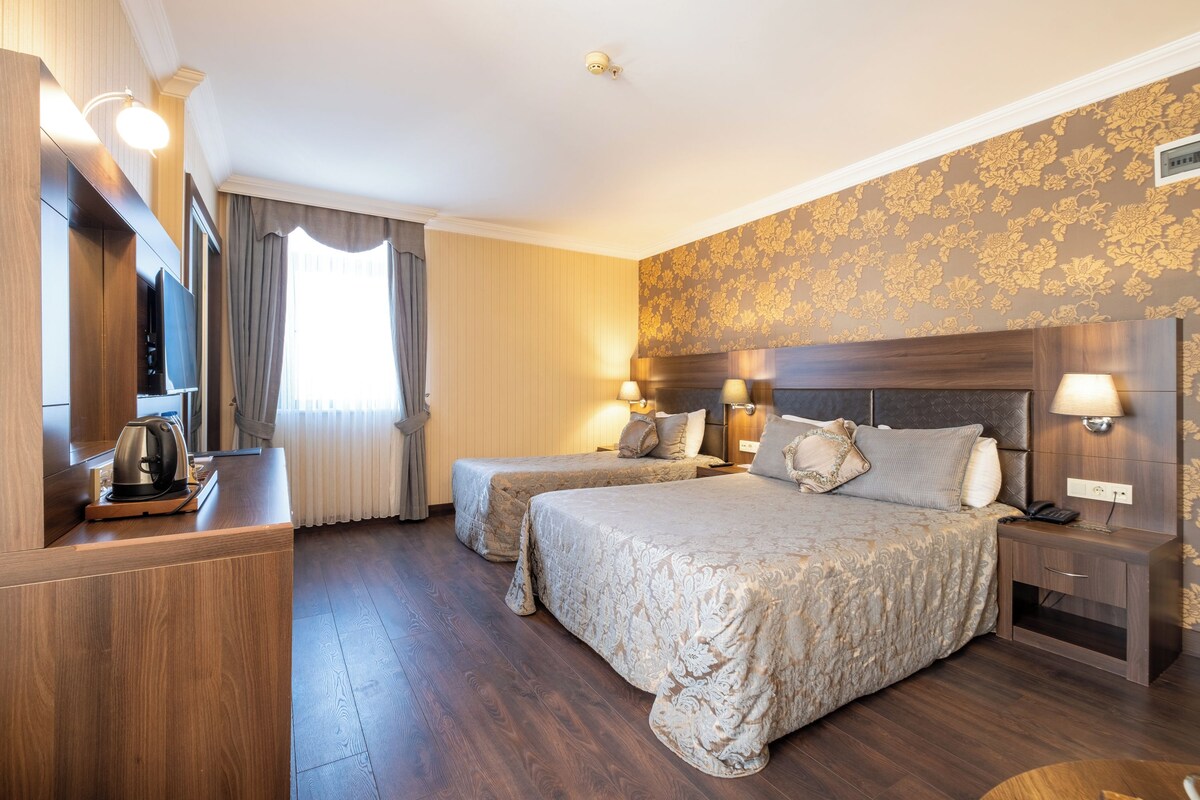 Habitación de hotel con dos camas, televisión, cafetera y mesita de noche.