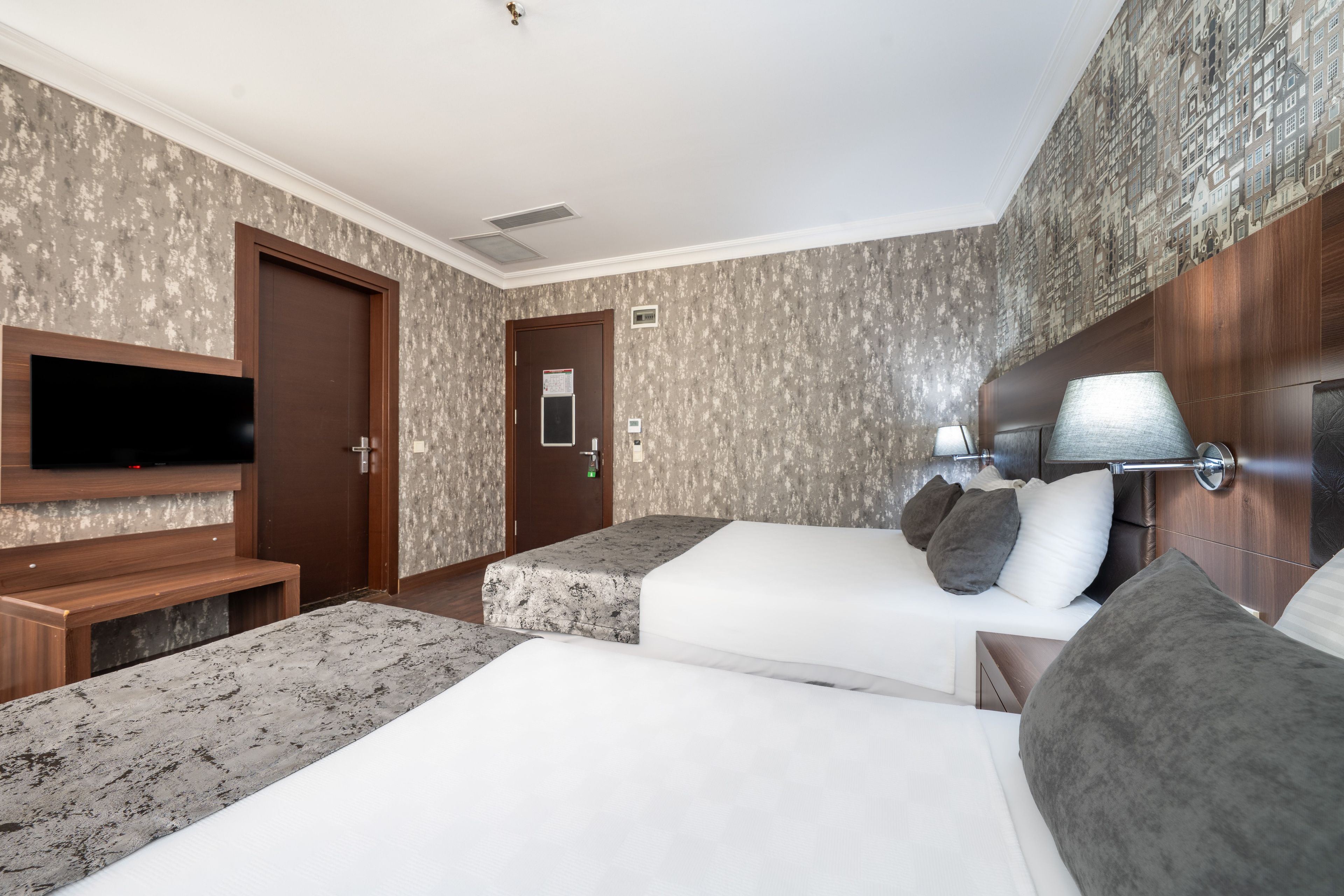 A hotel room with two beds, a TV, a desk, and a patterned wall.