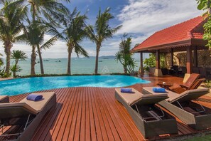 Terraza de madera con sillones de descanso y una piscina con vista al mar.