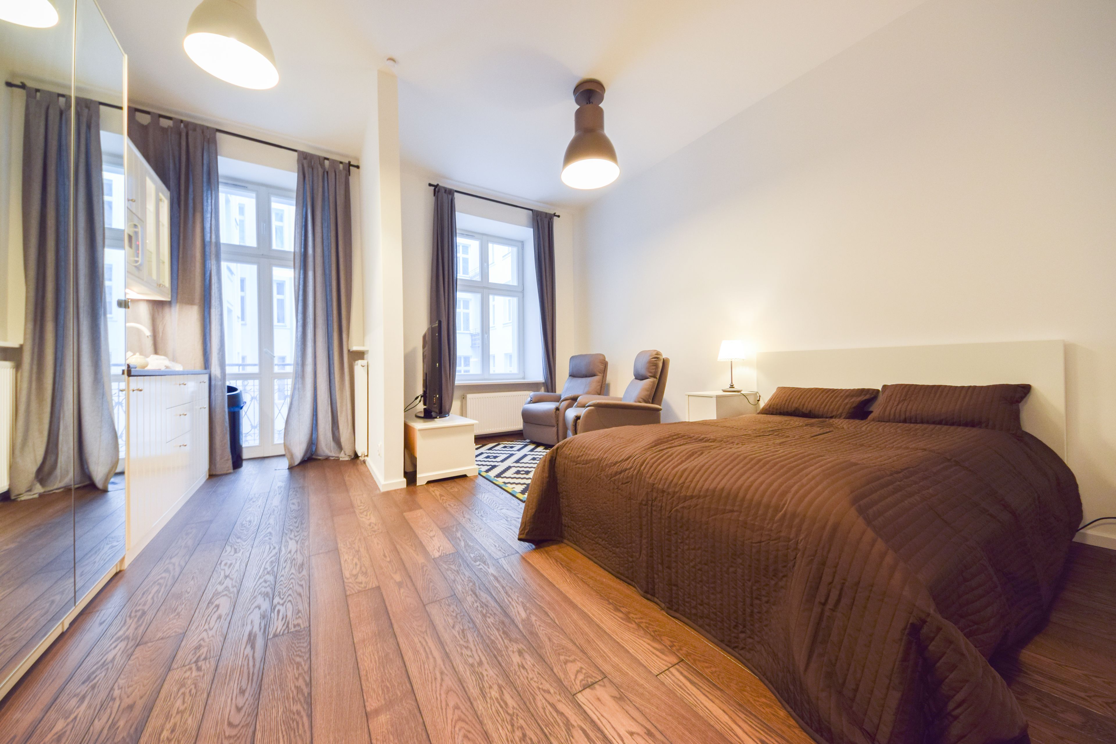 Une chambre d’hôtel avec un grand lit, une chaise, un bureau, un miroir et une fenêtre avec des rideaux.