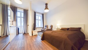 Ein Hotelzimmer mit einem großen Bett, einem Sessel, einem Schreibtisch, einem Spiegel und einem Fenster mit Vorhängen.