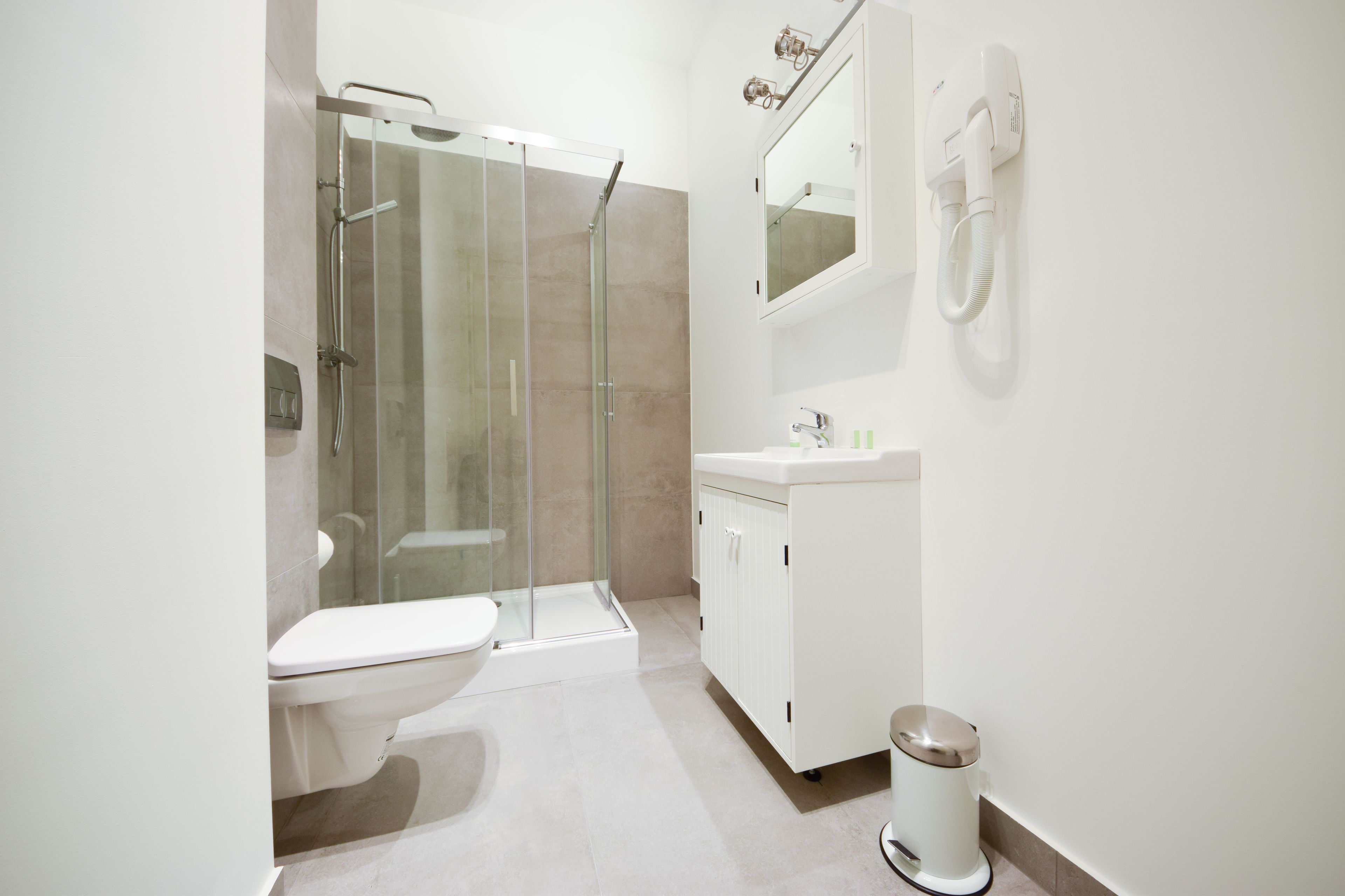 A modern bathroom with a glass-enclosed shower, a toilet, a sink, and a trash bin.