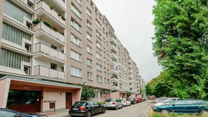 A multi-story residential building with a row of parked cars along a cobblestone street. - ShortStayPoland Jana Pawła - B27 (Warsaw)