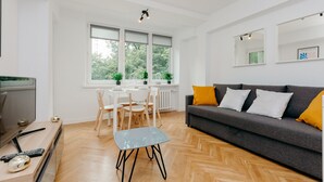A modern living room with a grey sofa, wooden floor, and a dining area with white chairs and a table. - ShortStayPoland Jana Pawła - B27 (Warsaw)