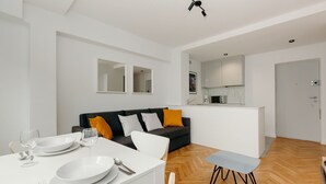 A modern living room with a dining area, a sofa with cushions, a kitchen area, and a door. - ShortStayPoland Jana Pawła - B27 (Warsaw)