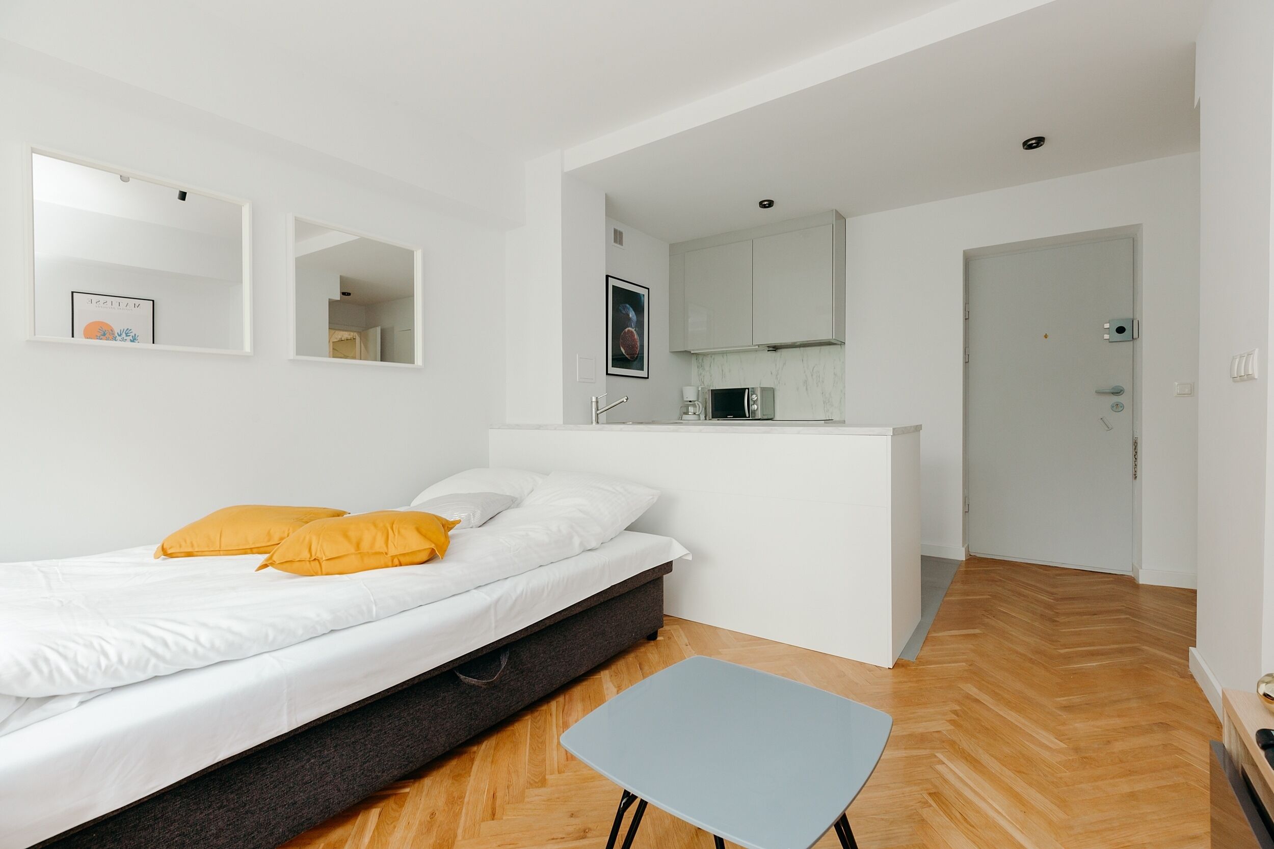 A modern bedroom with a bed, a small table, and a kitchenette area.