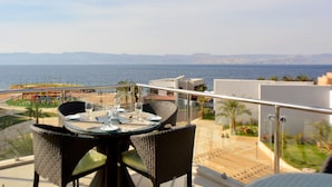 A balcony with a table set for dining, overlooking a beach and the sea. - Public Security Hotel & Chalets (Aqaba)