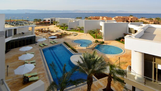 A resort with a swimming pool, lounge chairs, and a view of the sea. - Public Security Hotel & Chalets (Aqaba)