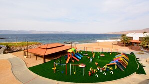 A playground with slides and swings, a covered seating area, and a view of the sea. - Public Security Hotel & Chalets (Aqaba)
