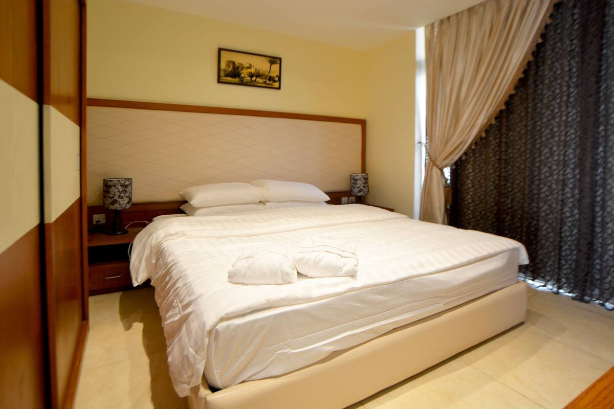 A neatly made bed with white linens, a headboard, and a bedside table with a lamp.
