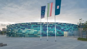 A modern building with a circular glass facade and three flags on flagpoles. - Rooms Rent Vesuvio B&B (Naples)