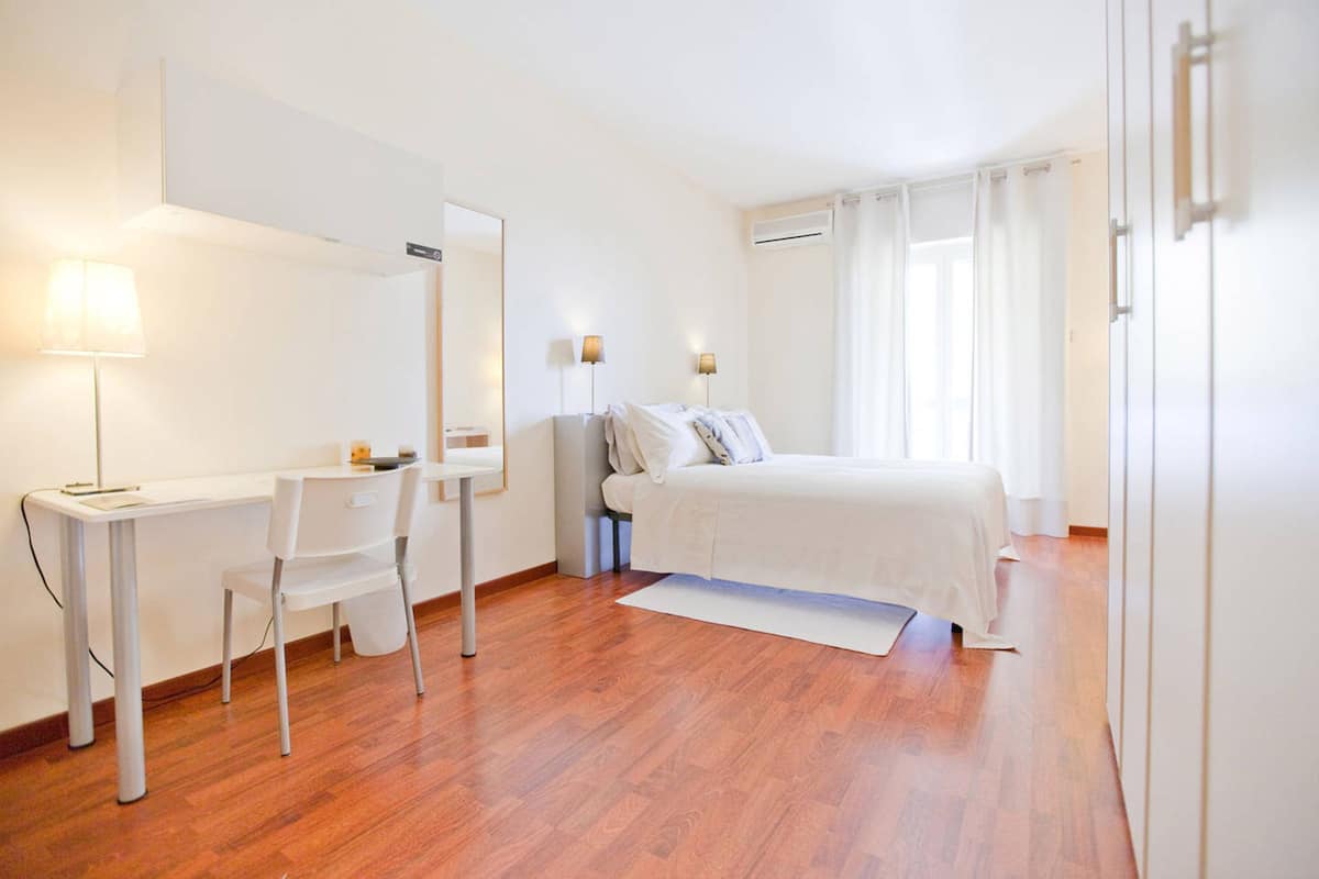 A hotel room with a bed, a desk, a chair, a mirror, and two bedside lamps.