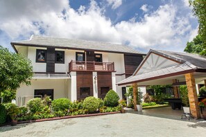 A two-story house with a balcony, a covered patio, and a garden with various plants.