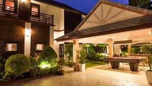 Un espacio exterior bien iluminado con mesa de billar, una zona de estar cubierta y un edificio con balcón.