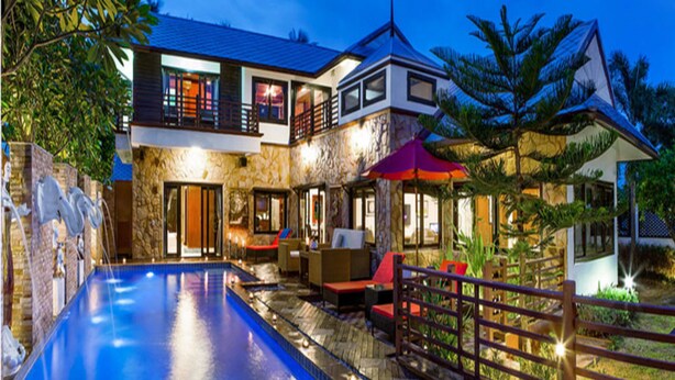 Una casa de dos pisos con piscina, mobiliario exterior y un paraguas rojo.