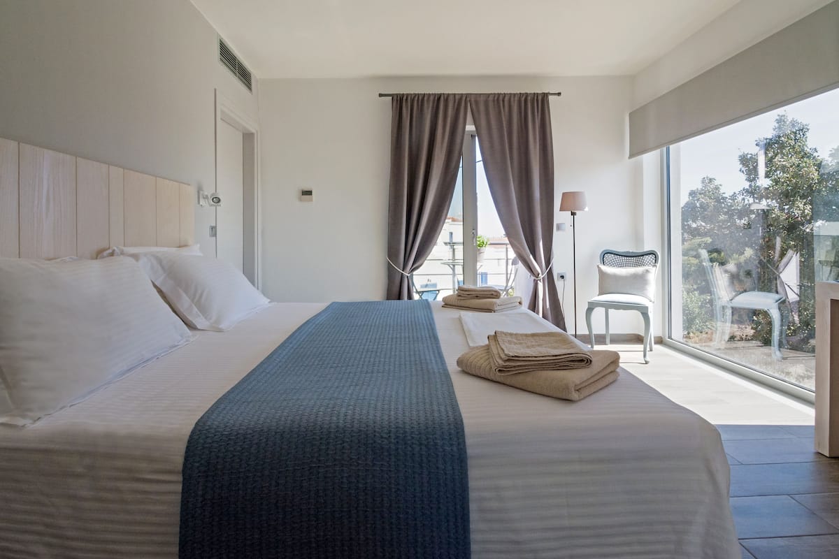 A hotel room with a large bed, a view of the outdoors, and a chair by the window.