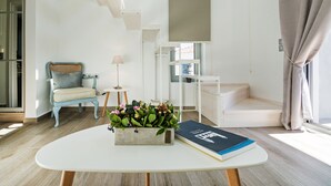 Ein modernes Wohnzimmer mit einem weißen Sofa, einem kleinen Beistelltisch mit einer Lampe, einem Couchtisch mit einer Blumenvase und einer Treppe, die zu einer oberen Ebene führt.