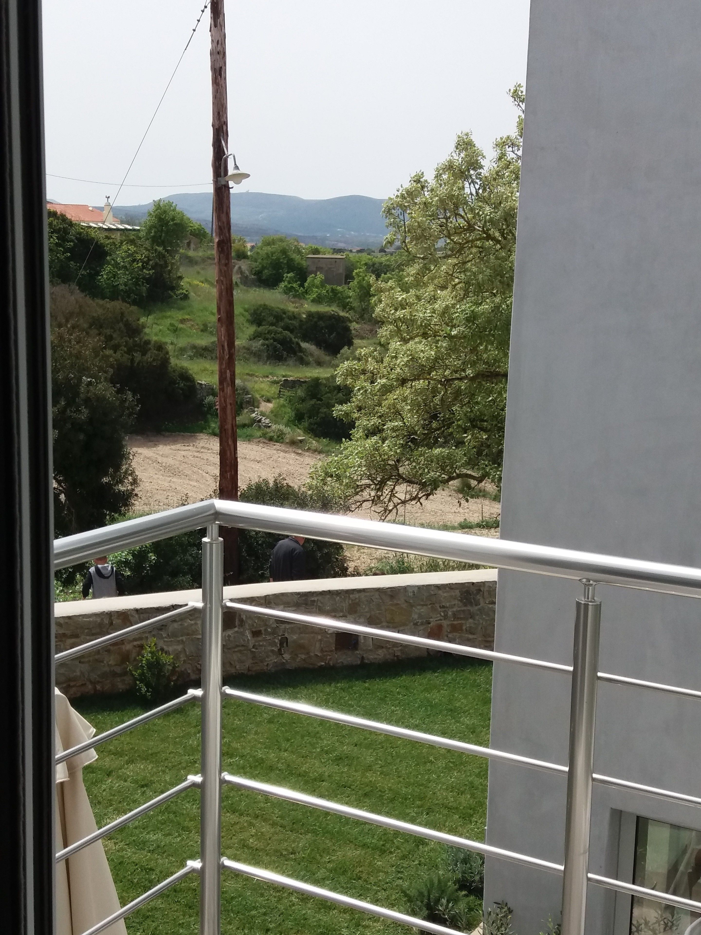 A balcony with a metal railing overlooking a grassy area with trees and a stone wall.