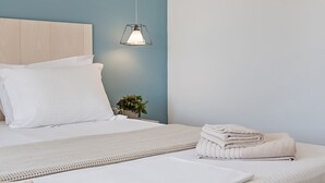 Ein ordentlich bezogenes Bett mit weißen Leinen, eine Nachttischlampe und ein kleiner Topf mit Pflanze auf dem Nachttisch.