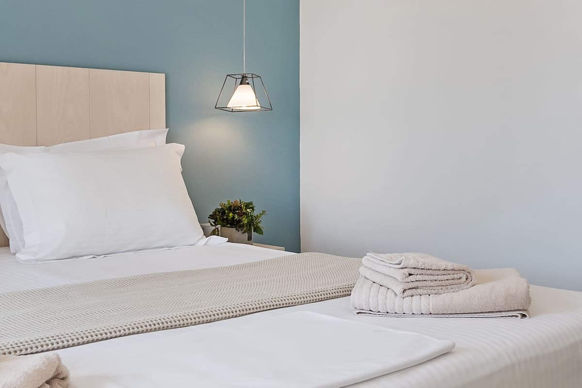 A neatly made bed with white linens, a bedside lamp, and a small plant on the nightstand.