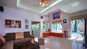 A spacious living room with a large sofa, a coffee table, and a view of a pool through the glass doors. - 4 Bedroomed Villa In Chaweng P1 SDV193 - By Samui Dream Villas (Koh Samui)