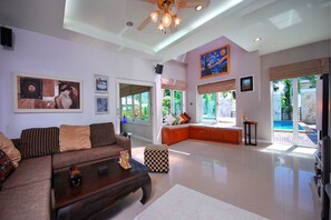 A spacious living room with a large sofa, a coffee table, and a view of a pool through the glass doors. - 4 Bedroomed Villa In Chaweng P1 SDV193 - By Samui Dream Villas (Koh Samui)