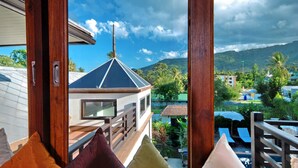 A balcony with colorful cushions, a view of a building with a pointed roof, and a pool area with lounge chairs. - 4 Bedroomed Villa In Chaweng P1 SDV193 - By Samui Dream Villas (Koh Samui)