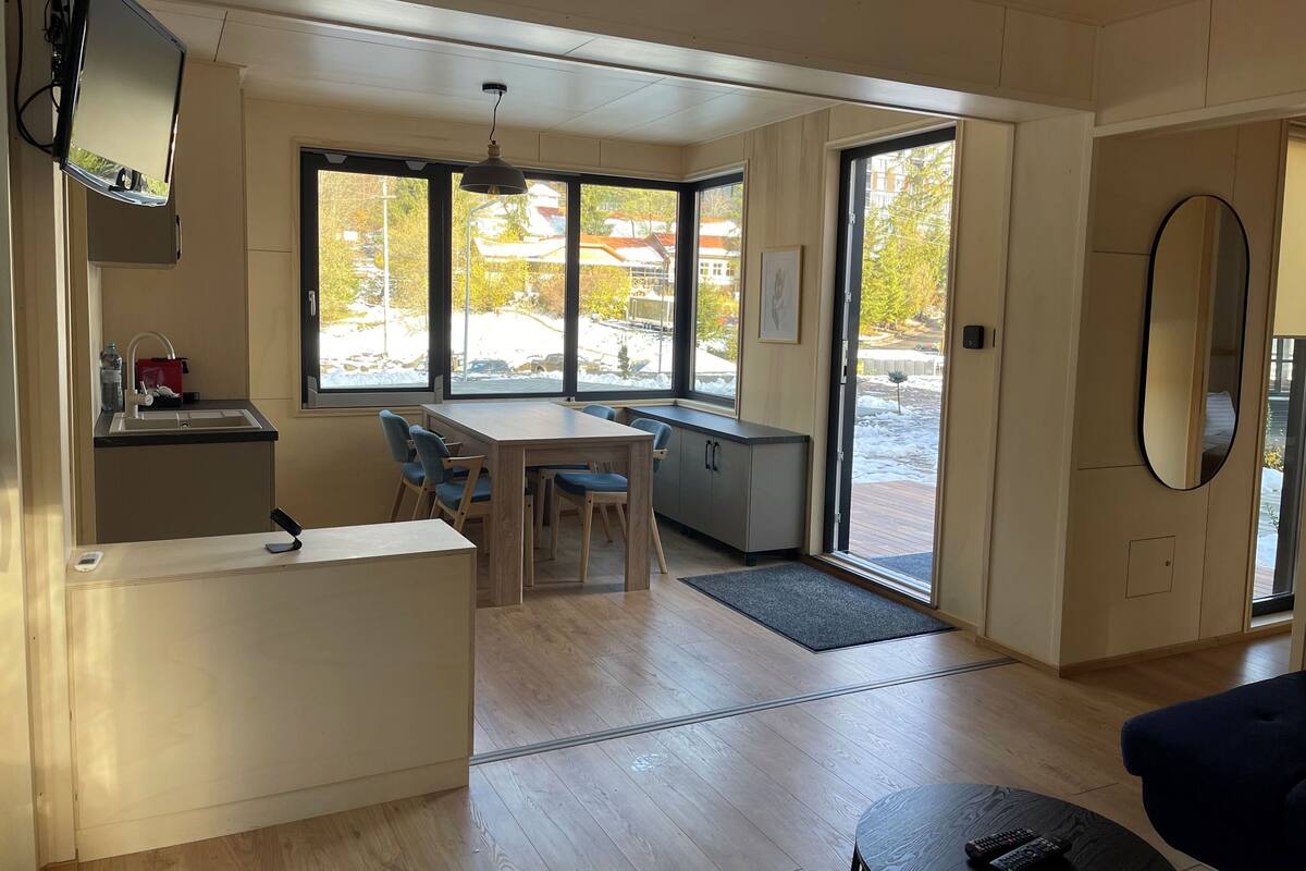 A modern kitchen with a built-in stove, a dining area with a table and chairs, and large windows offering a view of the outside.