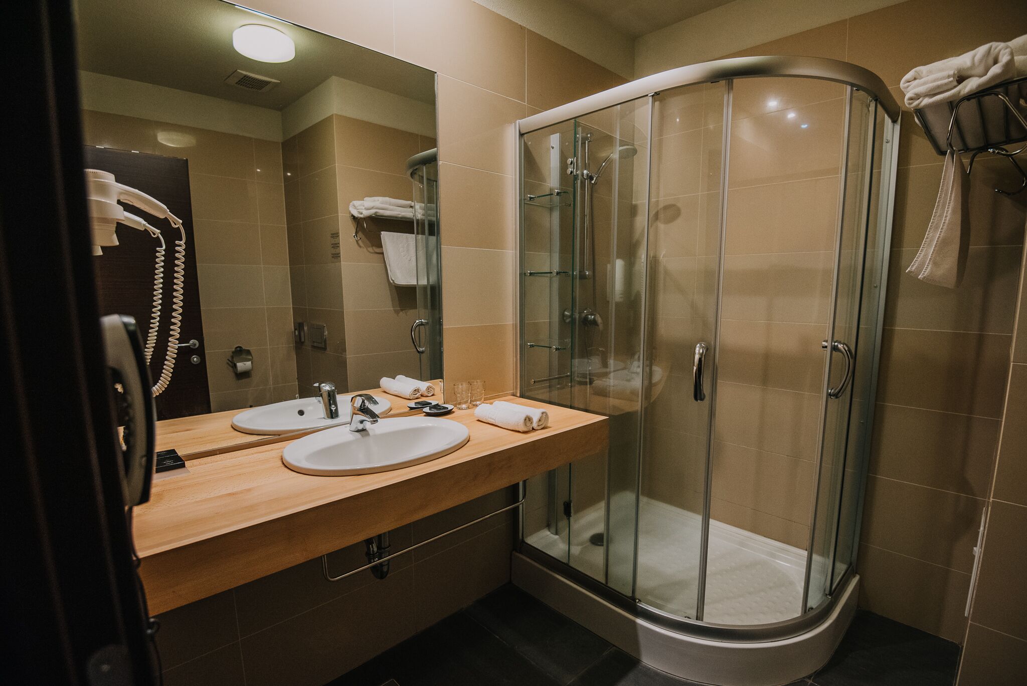 Een moderne badkamer met een douchecabine van glas, twee wastafels en een spiegel.