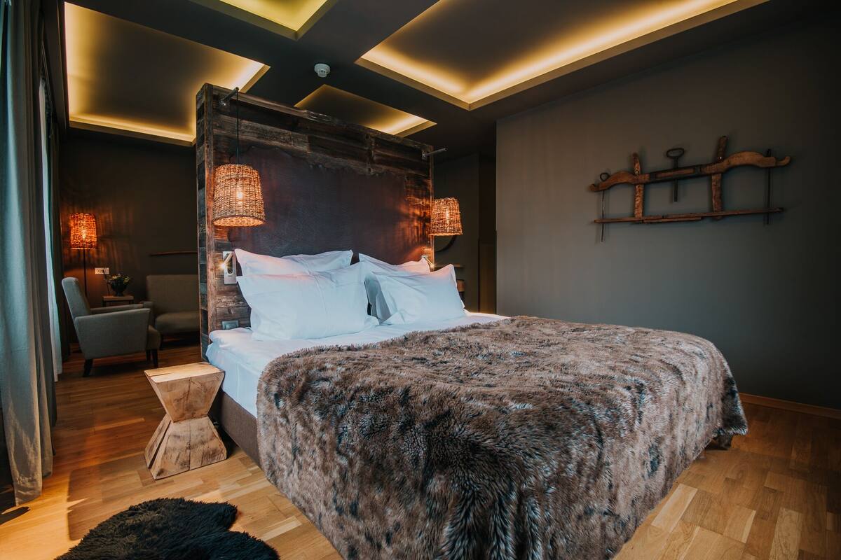 A modern bedroom with a large bed, wooden headboard, and ambient lighting.