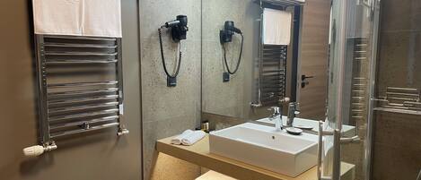 Un baño moderno con cabina de ducha de vidrio, un espejo grande y un perchero con toallas dobladas.