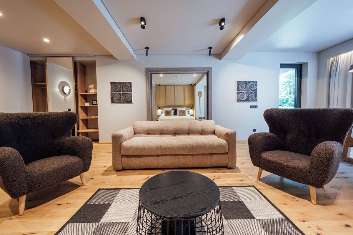 A modern living room with a sofa, two armchairs, a coffee table, and a wooden floor.