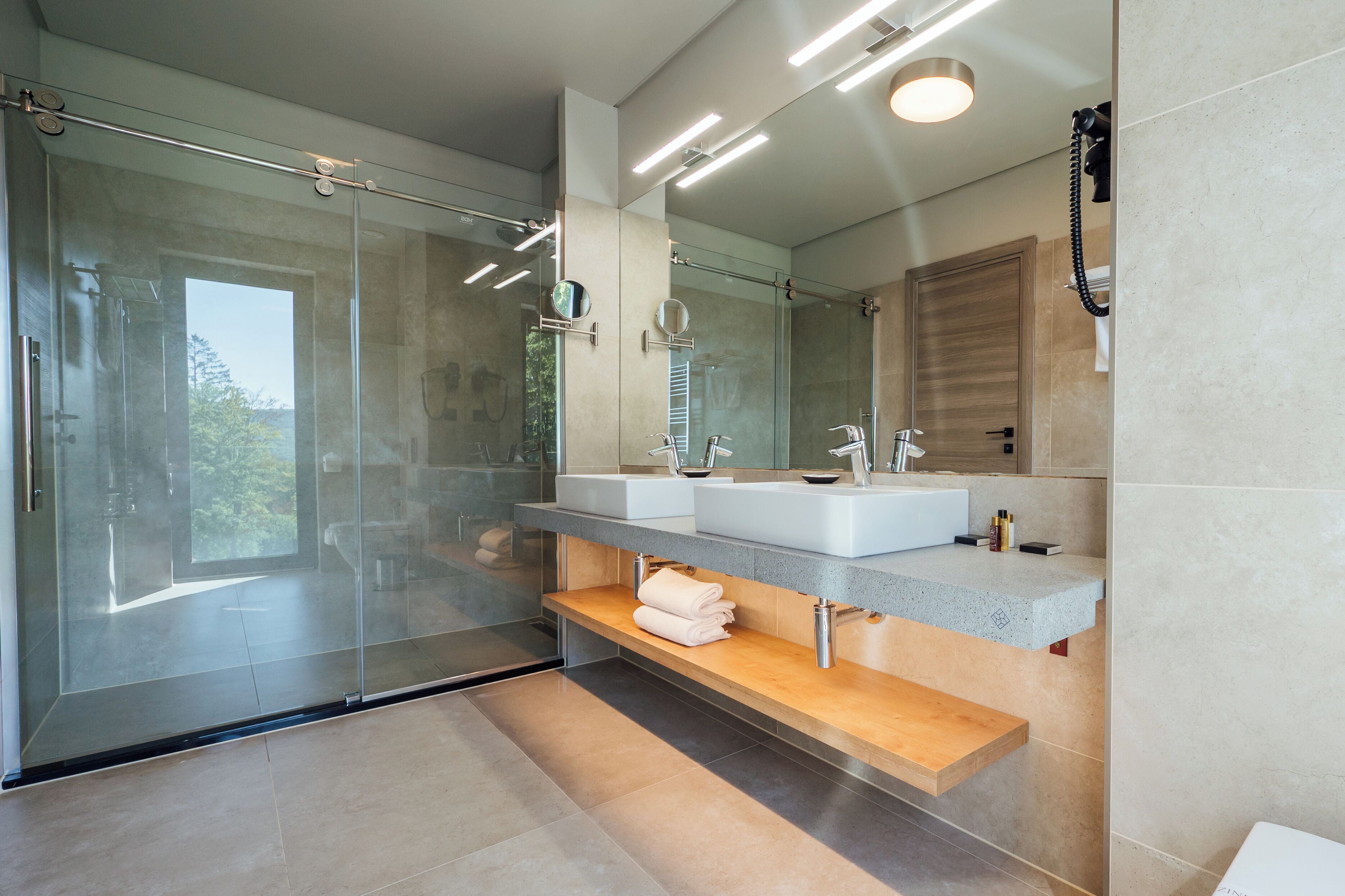 A modern bathroom with a glass-enclosed shower, dual sinks, and a large mirror.