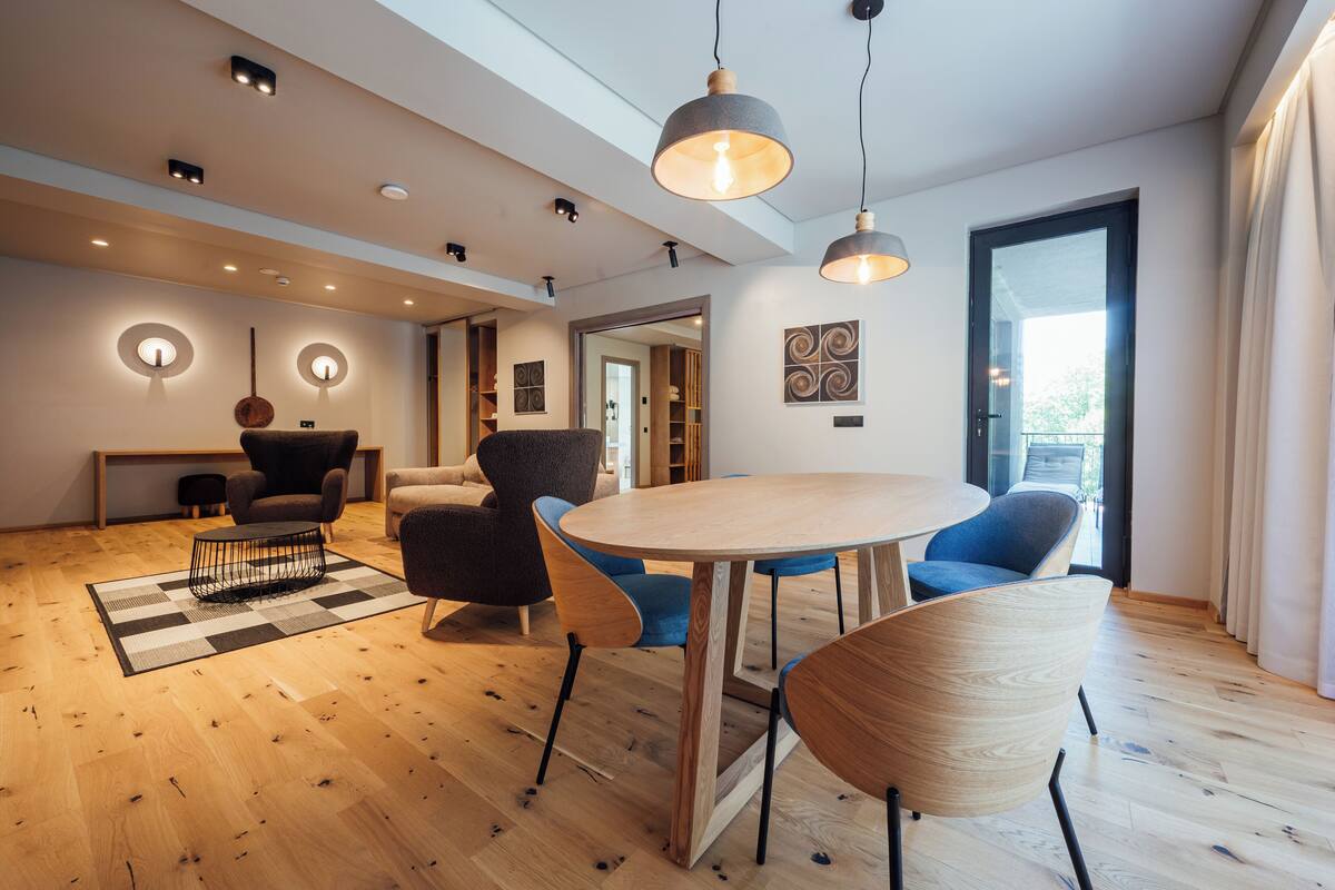 A modern living room with a round wooden table, blue and brown chairs, and pendant lighting.