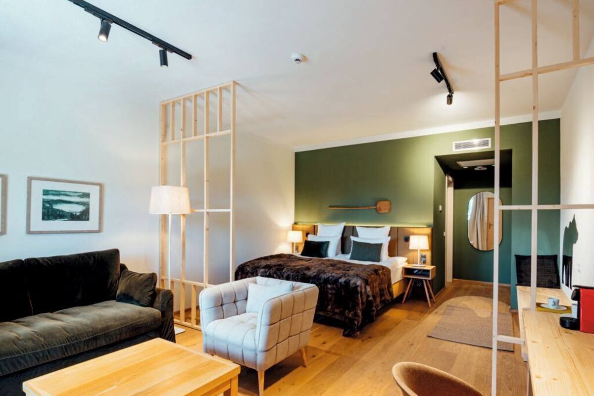 A modern hotel room with a bed, a sofa, a chair, a desk, and a mirror.