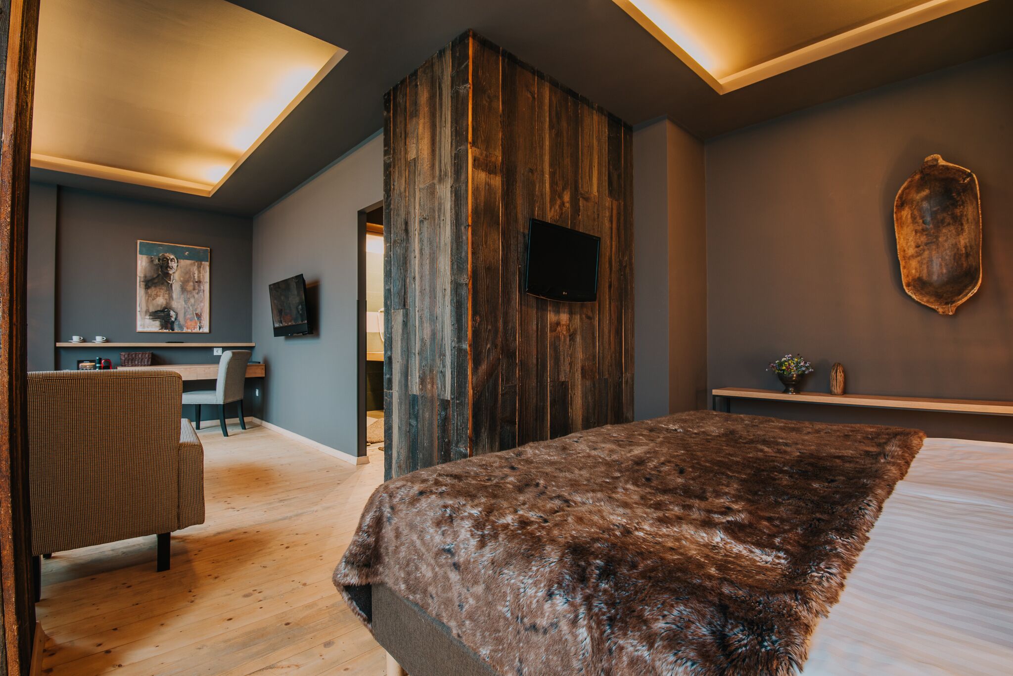 Een moderne slaapkamer met een houten accentmuur, een groot bed, een bureau en een televisie.
