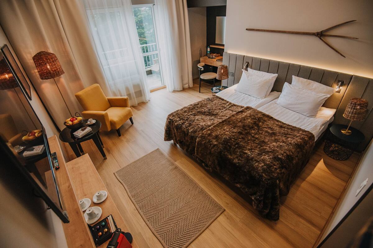 A modern hotel room with a large bed, a desk, a chair, and a view of the outdoors.