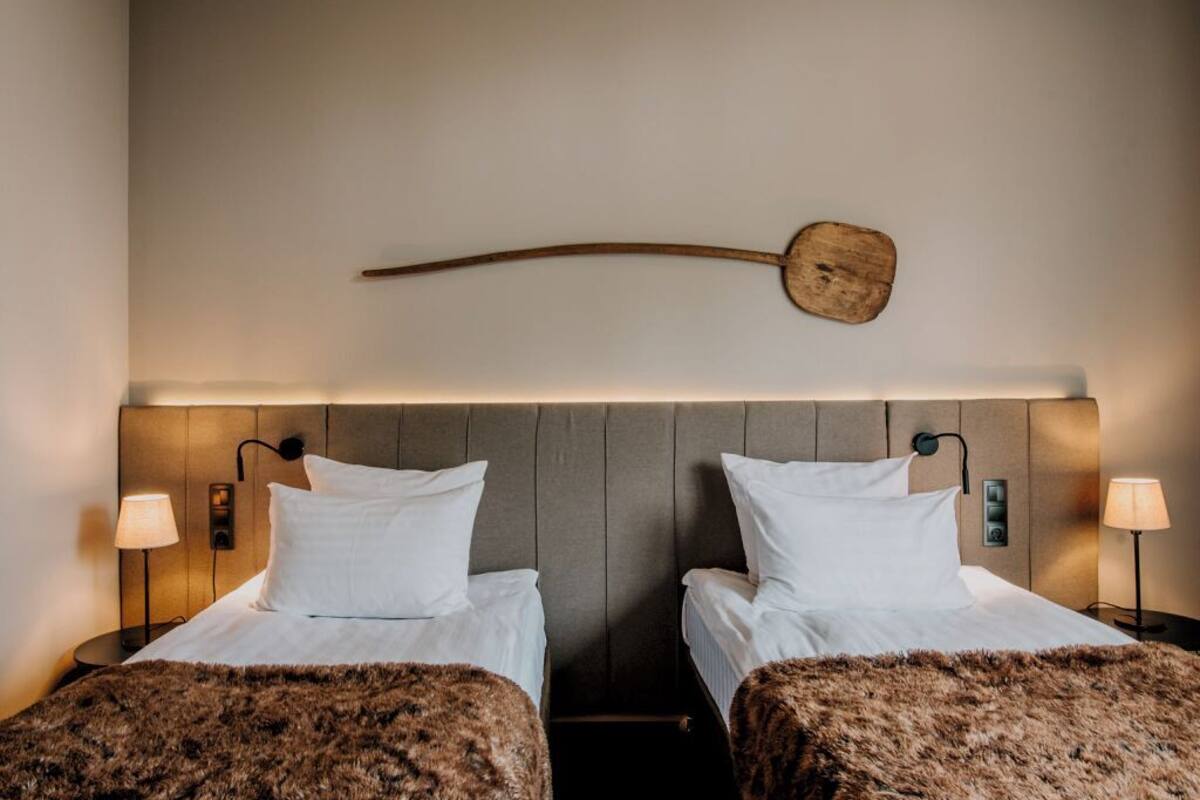 A hotel room with two beds, a wooden wall decor, and bedside lamps.