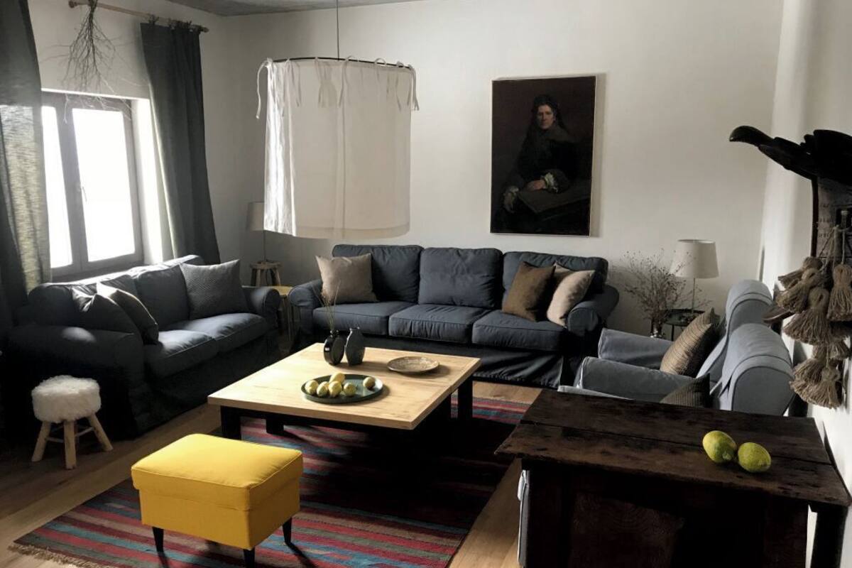 A living room with a dark blue sofa, a yellow ottoman, a wooden coffee table, and a striped rug.