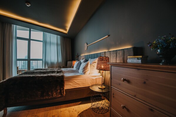 A modern bedroom with a large bed, bedside tables, a dresser, and a window with curtains.
