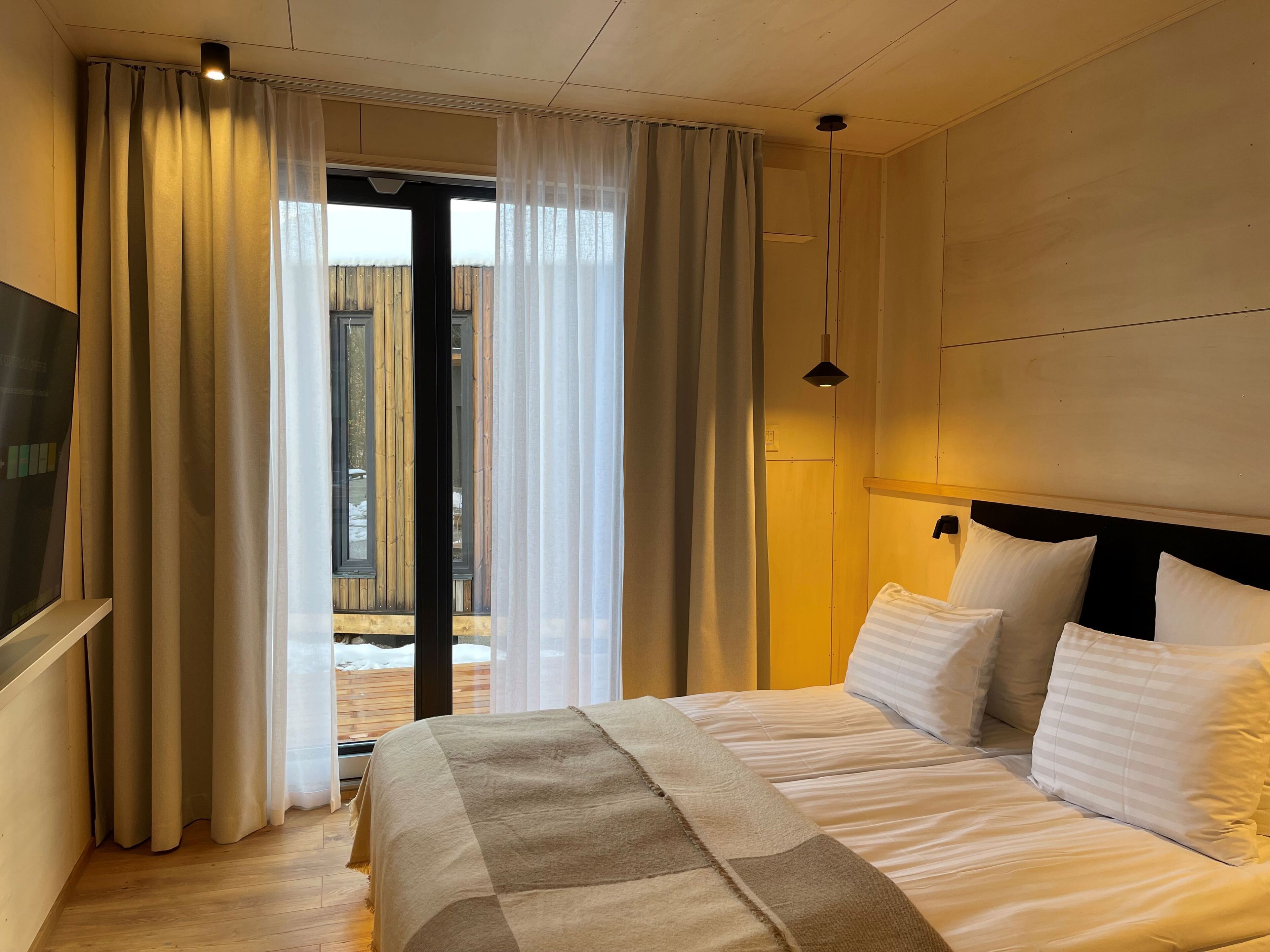 Habitación de hotel con cama, cortinas, televisión y vista al exterior.