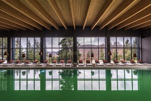 A poolside area with sun loungers and large windows offering a view of trees and mountains.