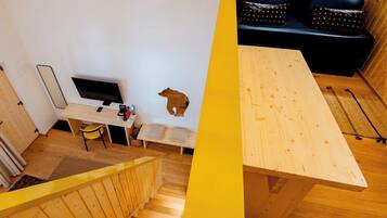 A modern interior with a wooden staircase, a dining area with a table and chairs, a black sofa with patterned cushions, and a small wooden sculpture.