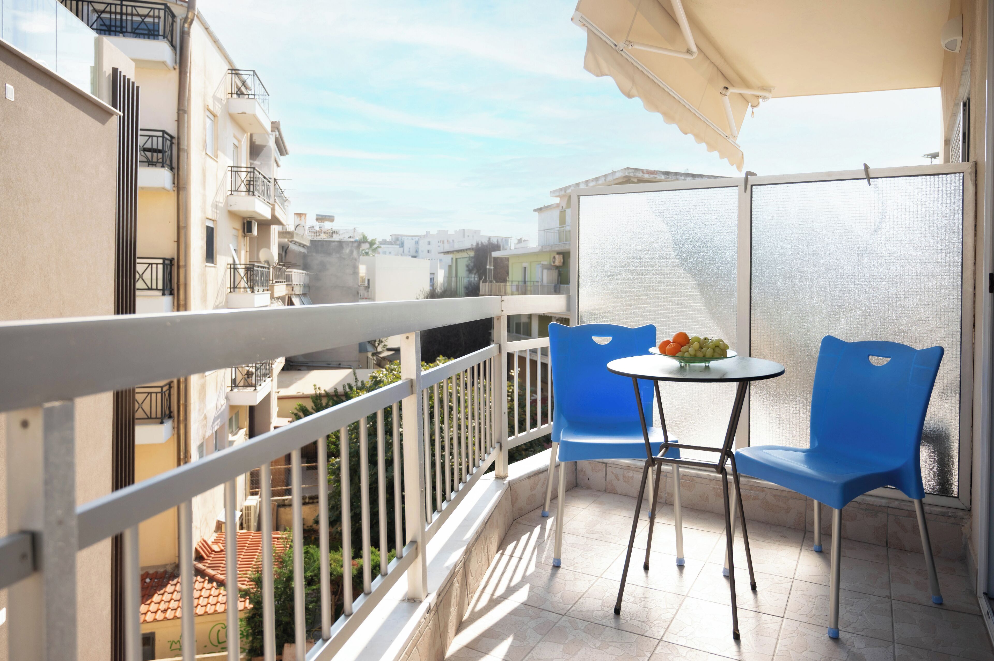 A balcony with a table and chairs, a view of the city, and a building with balconies.